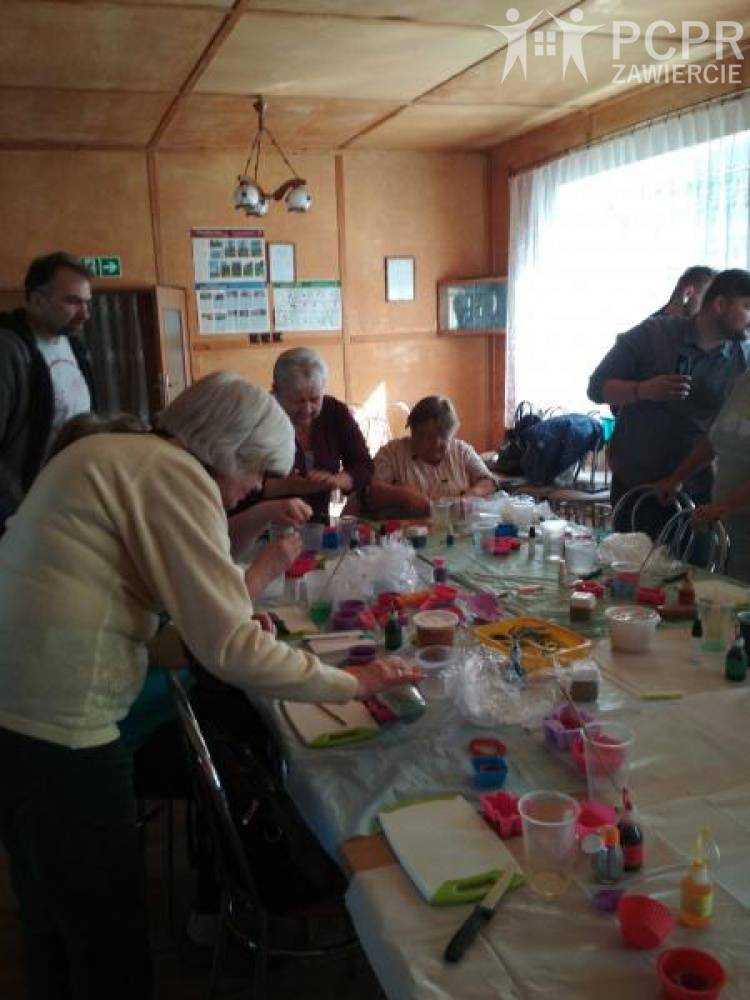 Zdjęcie: Kobiety i mężczyźni siedzą i stoją wokół stołu, na którym leży wiele plastikowych kubków, kolorowych foremek, fiolek, folii
